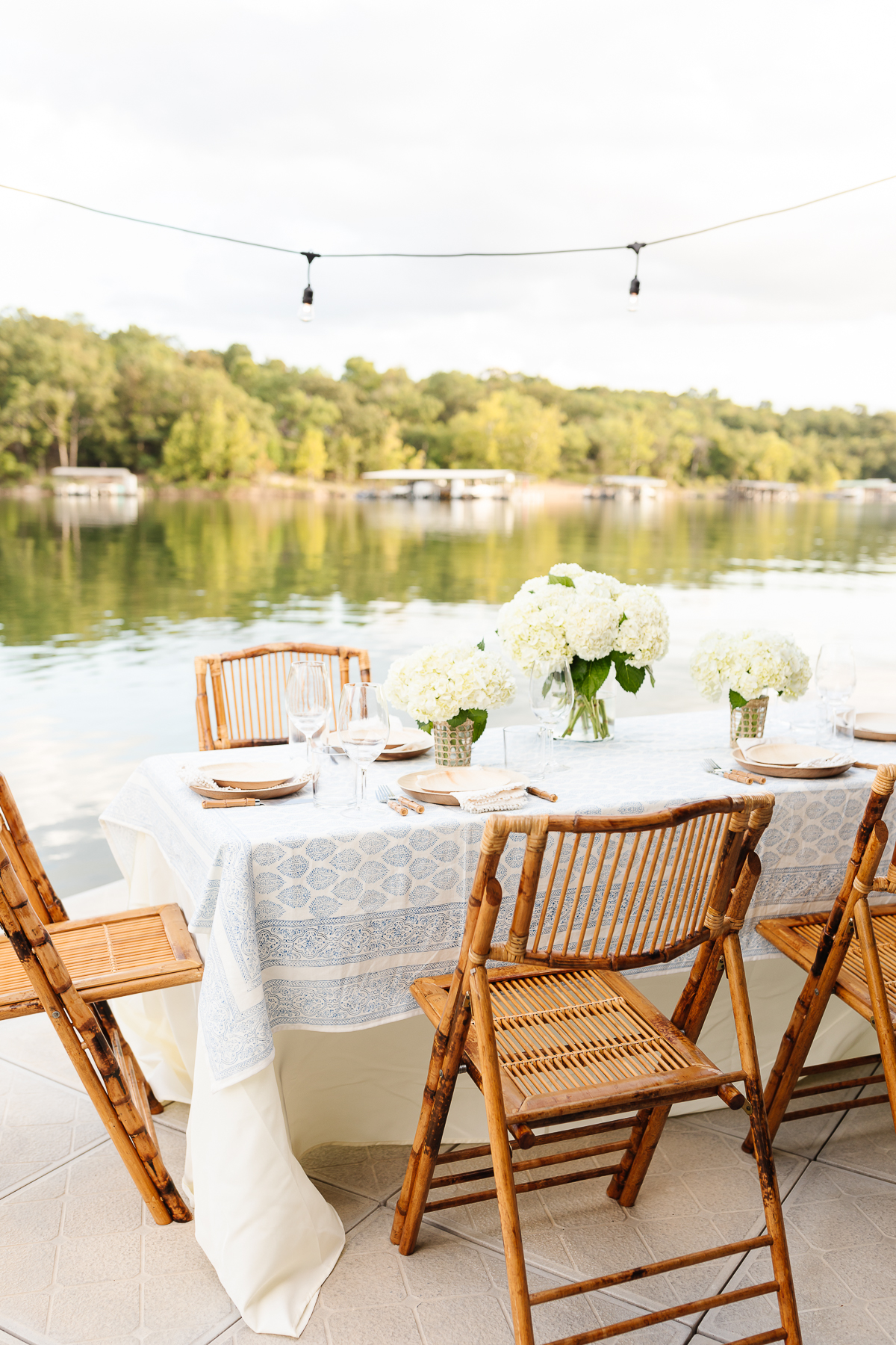 A table set up with white flowers, illuminated by the outdoor lighting with a lake in the background.