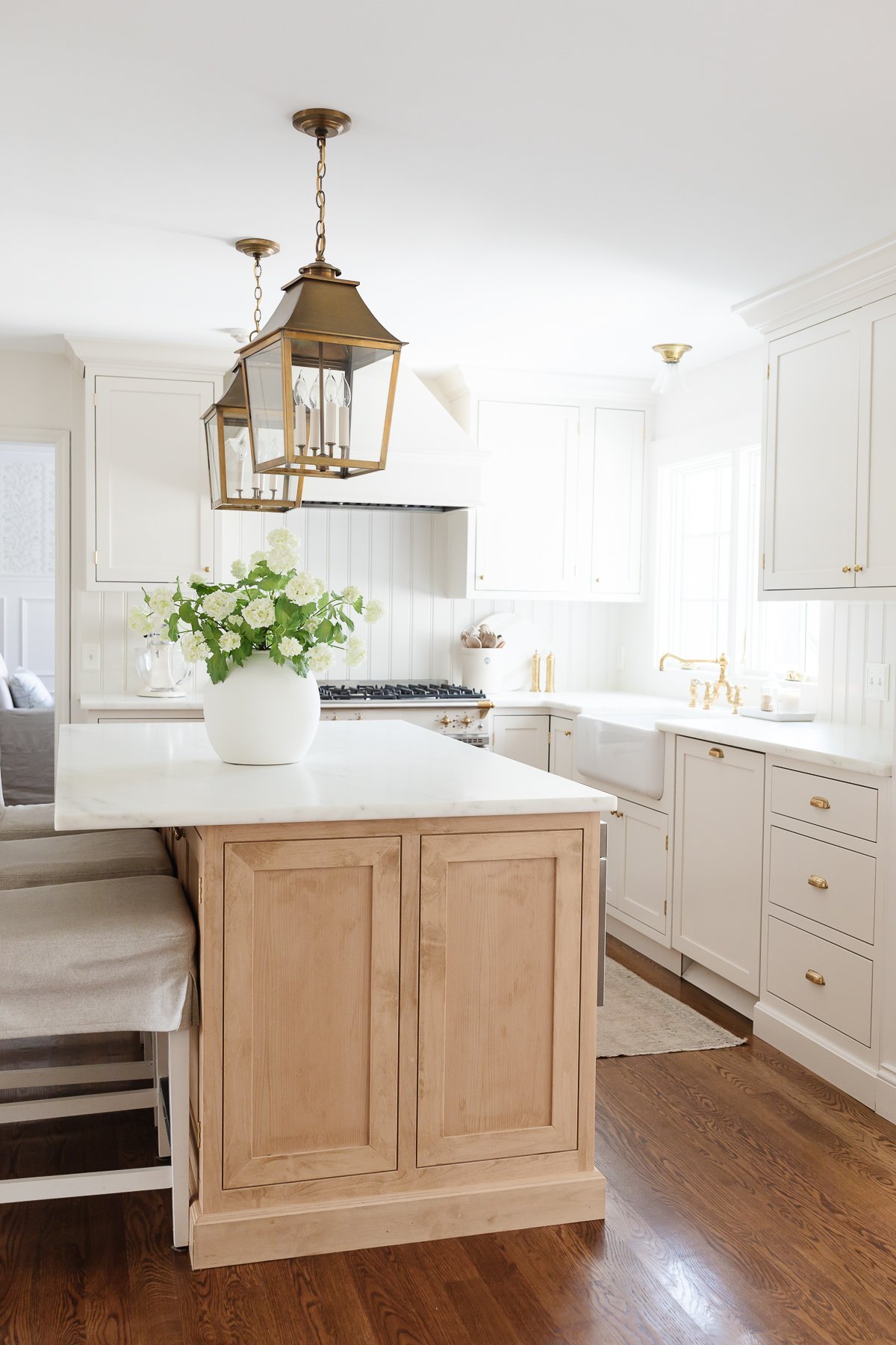 a white kitchen with brass lanterns over the island