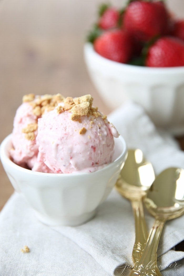 A white bowl filled with a no churn ice cream recipe, gold spoons and strawberries to the side.
