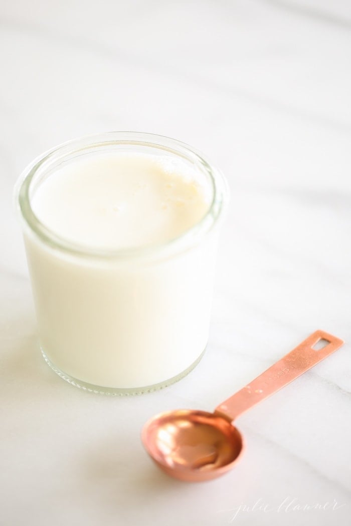 Homemade buttermilk substitute in a small glass jar with a copper measuring spoon nearby.
