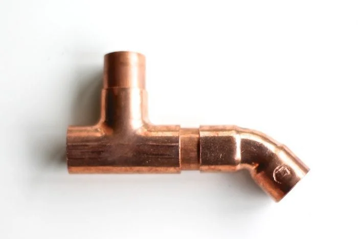 A copper pipe fitting with a T-shape and an angled joint is placed on a white background, perfect for DIY copper curtain rods.