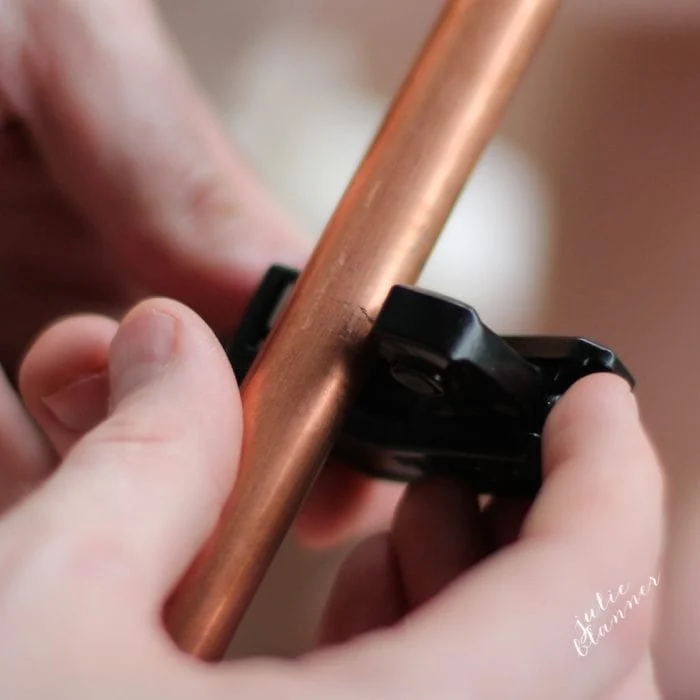 Two hands are using a pipe cutter tool to cut a copper pipe, perfect for crafting DIY copper curtain rods.