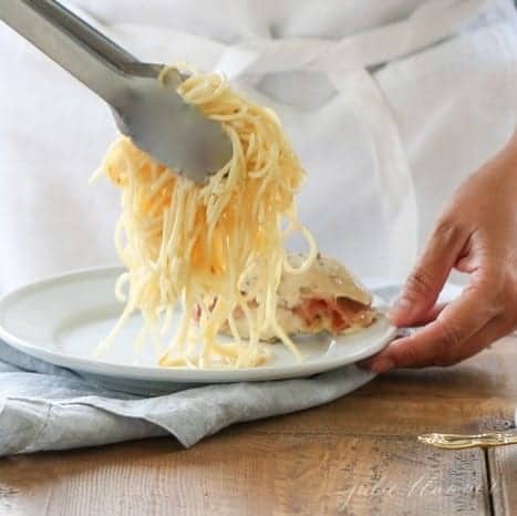A helping of fontina pasta being served onto a white plate with silver tongs.