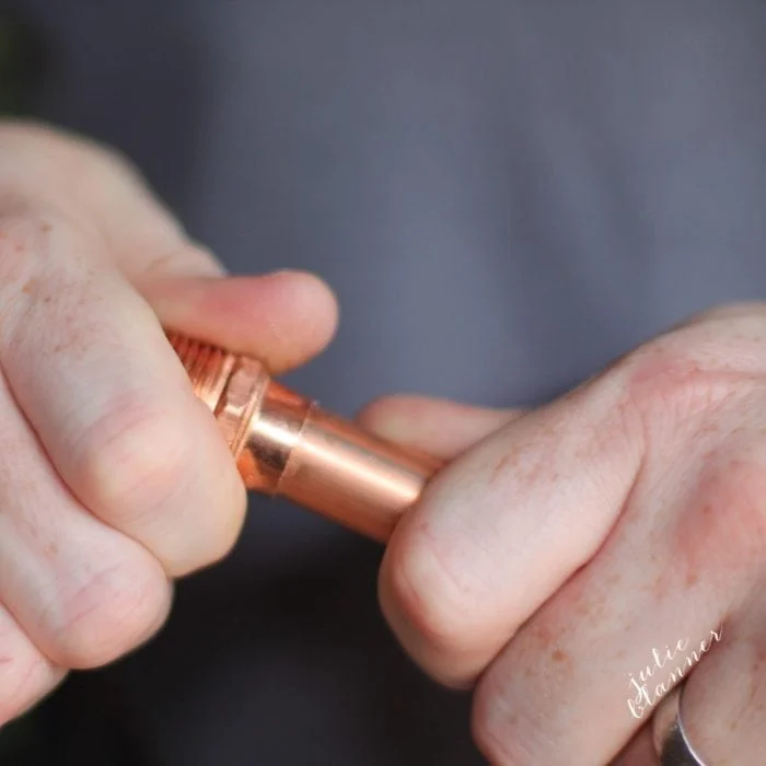 Close-up of hands twisting a copper pipe fitting, perfect for creating DIY copper curtain rods.