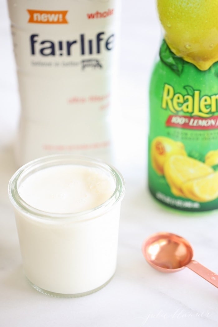 Homemade buttermilk in small glass jar in front of milk carton and bottle of lemon juice