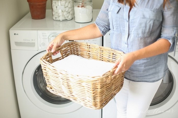 woman carrying basket of laundry in front of laundry machine