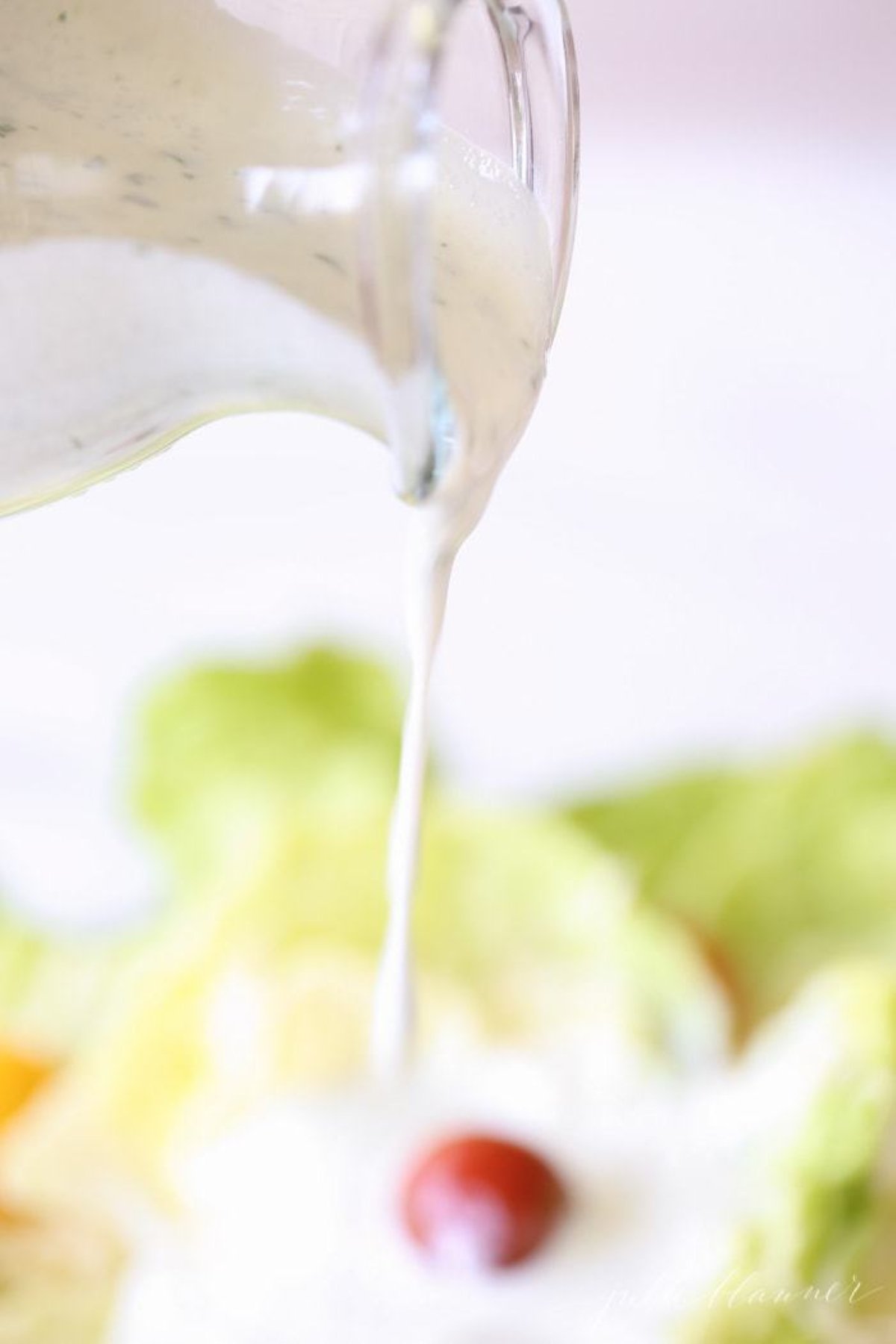 A clear glass bottle of homemade ranch dressing pouring over a salad