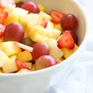 A bowl of easy vanilla fruit salad containing strawberries, grapes, and diced mango.