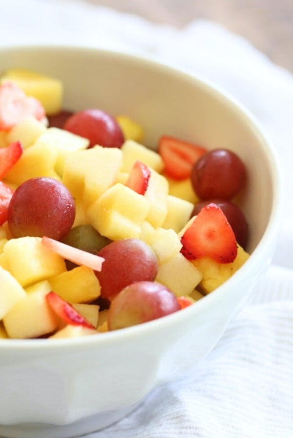 A bowl of easy vanilla fruit salad containing strawberries, grapes, and diced mango.