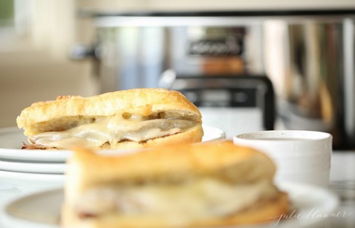 two classic French dip sandwiches with provolone cheese with Crockpot in background