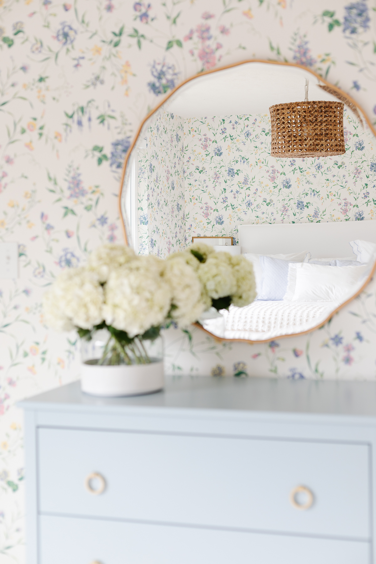 A dated blue dresser with floral bedroom wallpaper and a mirror.
