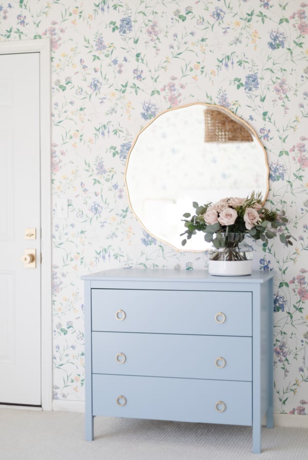 A blue dresser with bedroom wallpaper and a mirror.