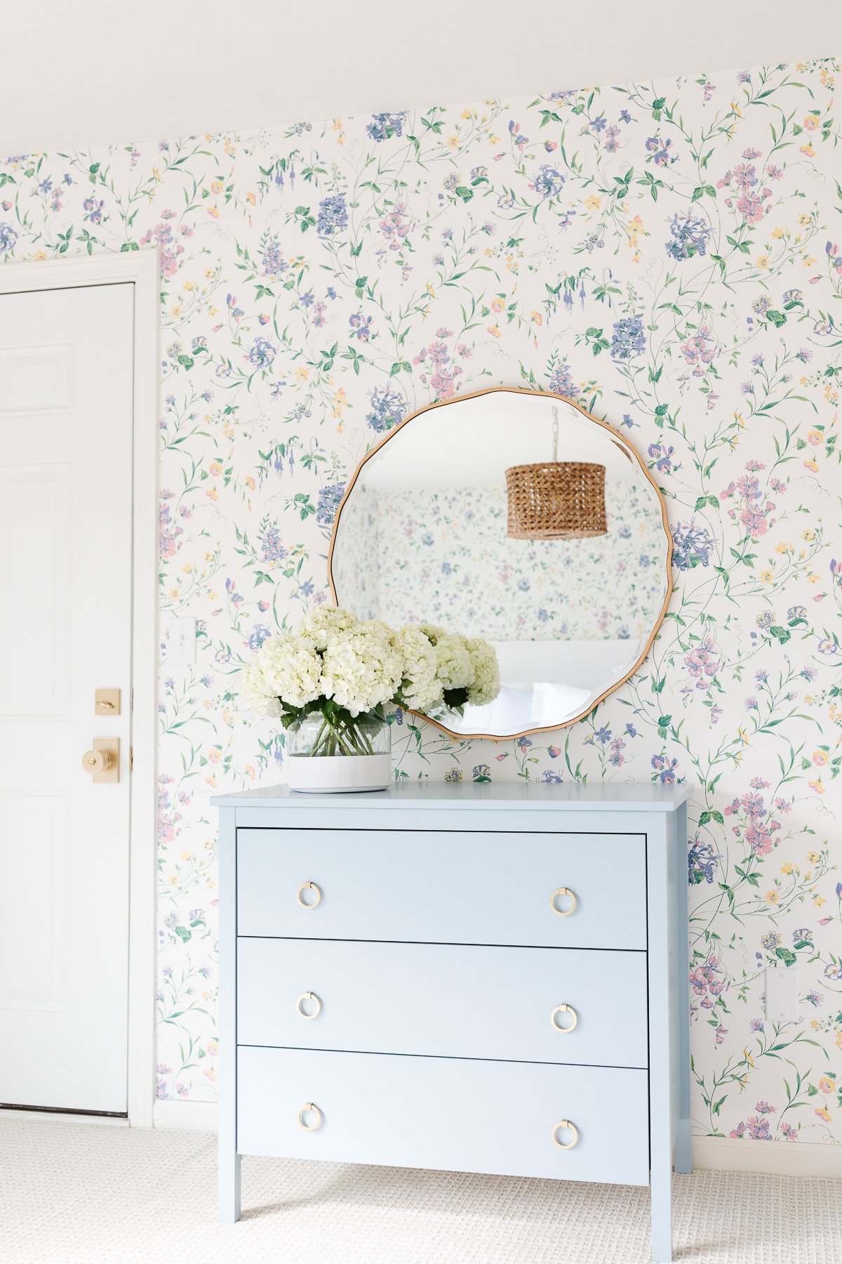 A bedroom with a blue dresser and dated floral wallpaper.