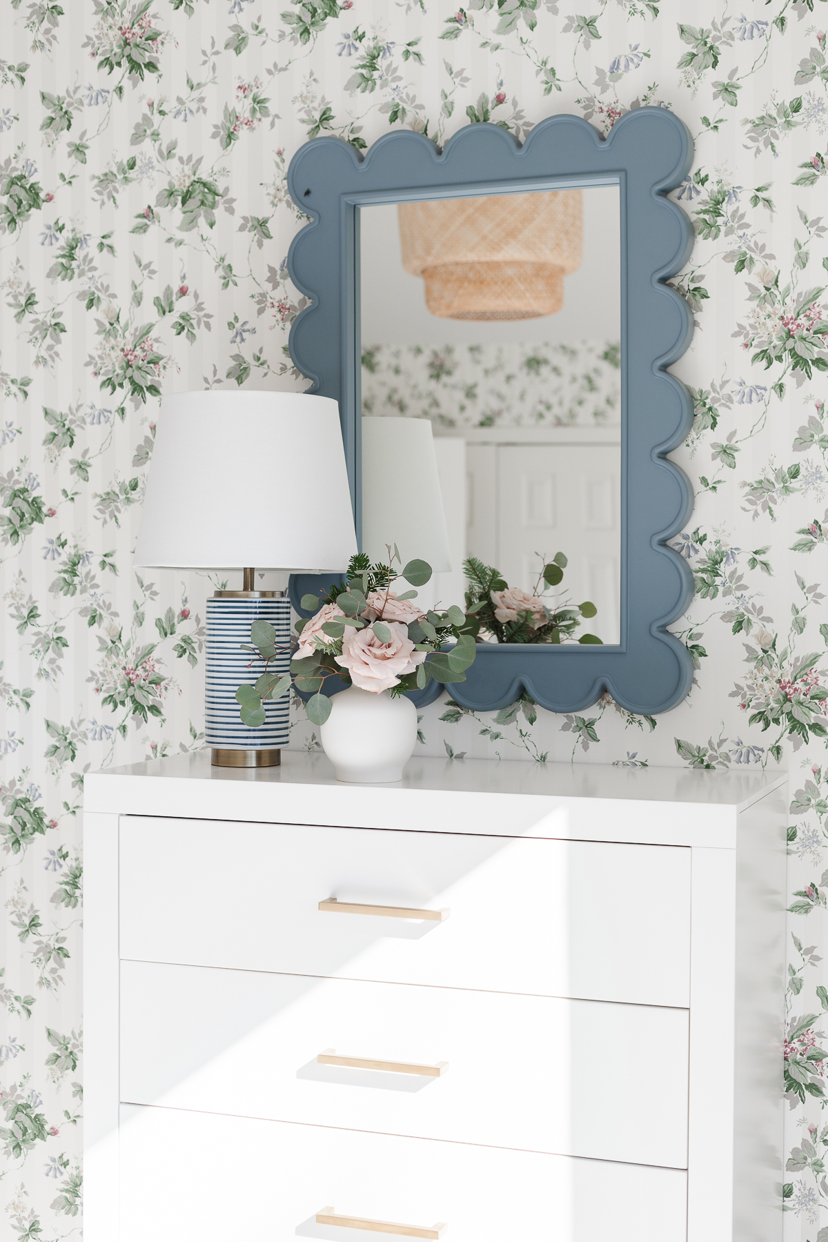 A bedroom dresser with a floral wallpaper and a mirror.