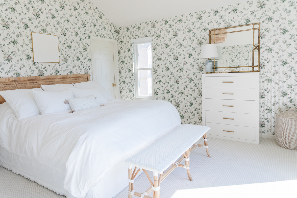 A white bedroom with dated floral wallpaper.