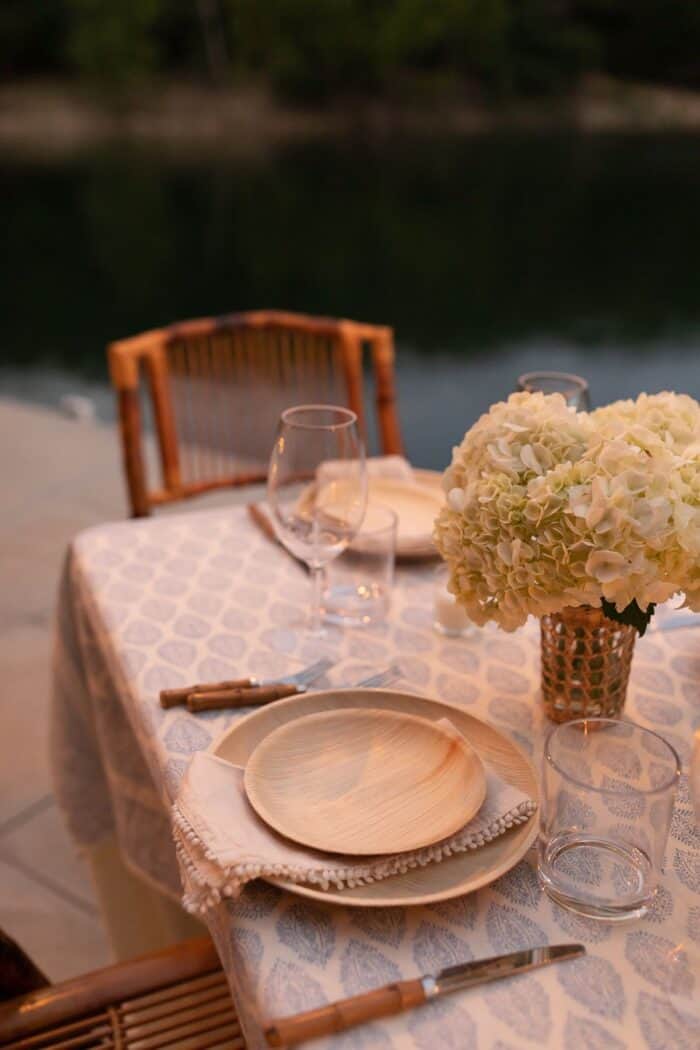A table set with rattan folding chairs and white flowers for dinner al fresco on a dock.