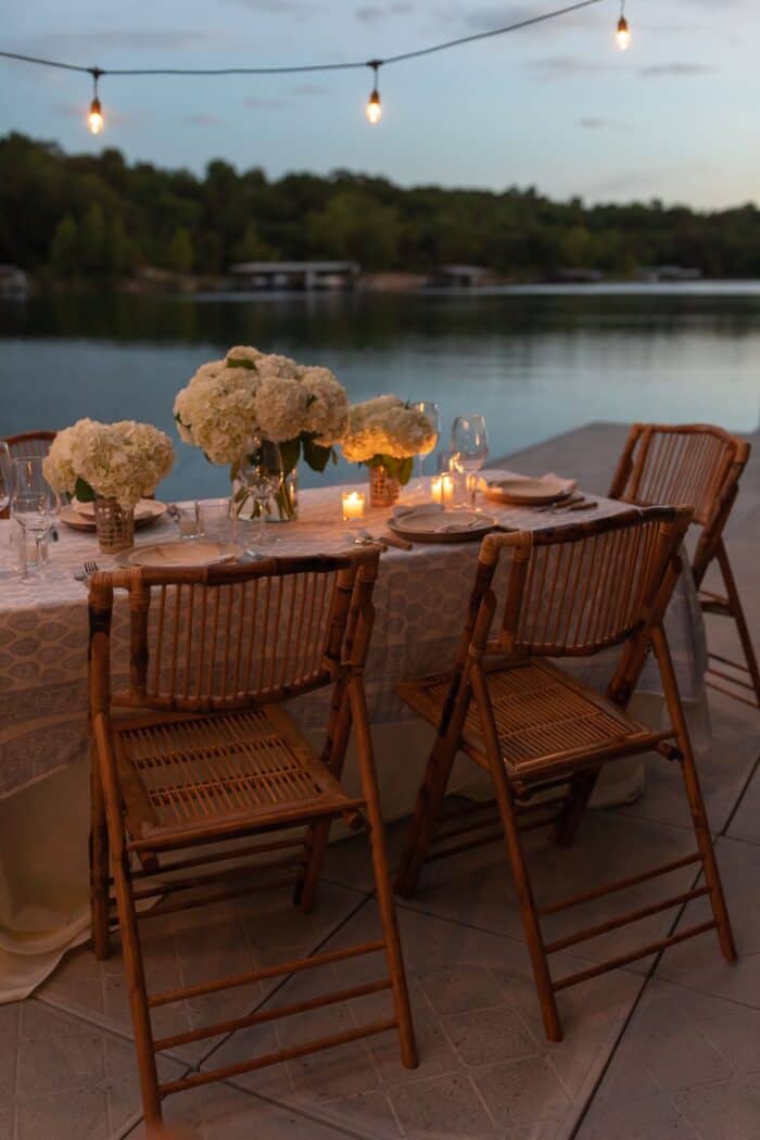 fall decorating for alfresco dining A table set with rattan folding chairs and white flowers for dinner al fresco on a dock.