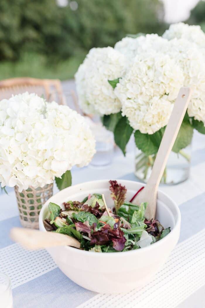 White hydrangea vases next to a salad bowl set up for dinner al fresco