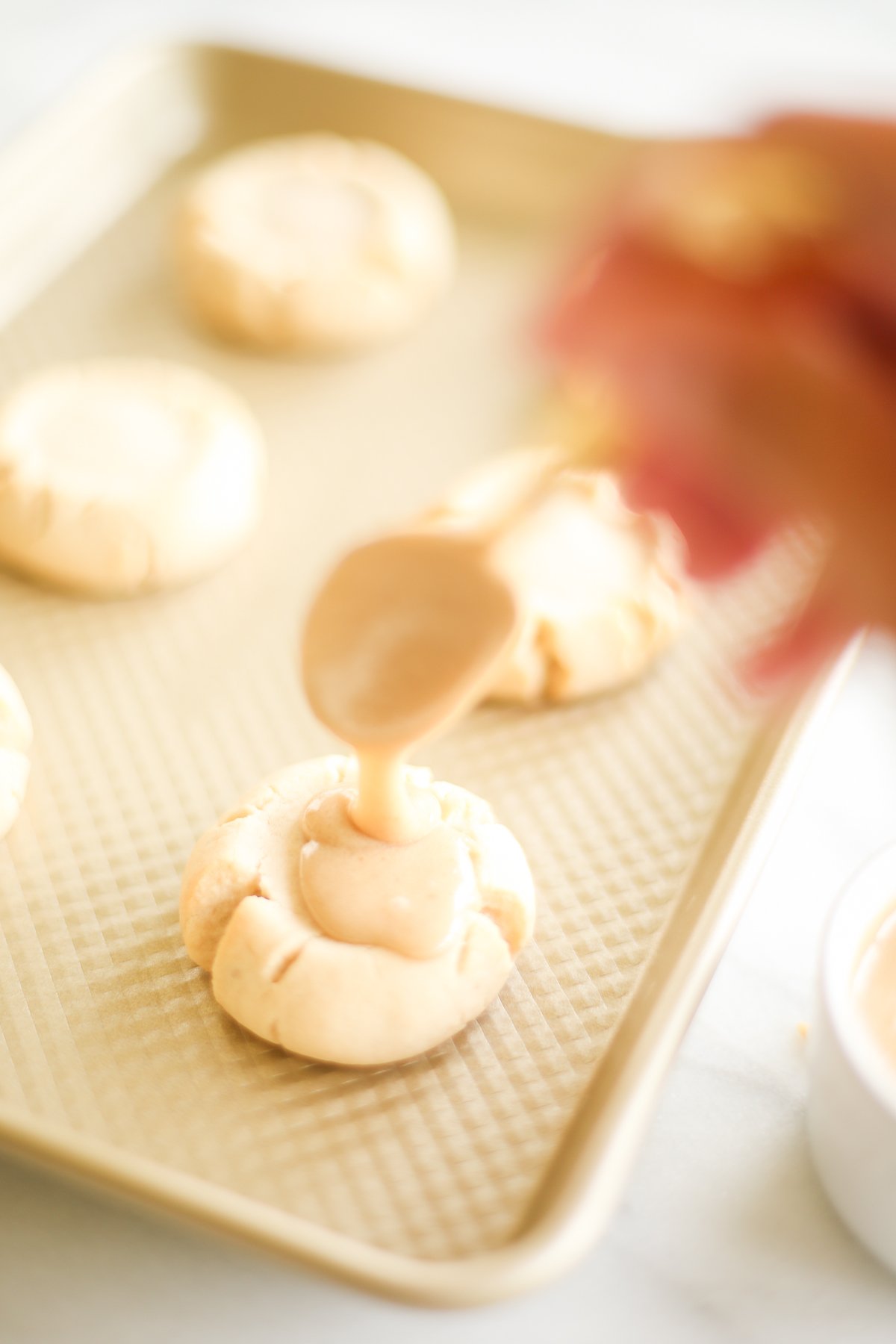 A person drizzling a caramel sauce on a baking sheet to create delicious caramel sugar cookies.