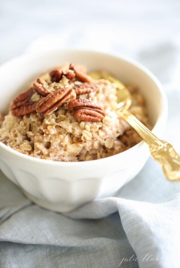 apple pie oatmeal in a white bowl with a gold spoon