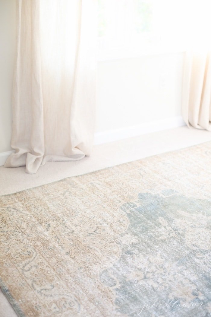 A white bedroom with a vintage turkish rug on carpet for a layered effect.