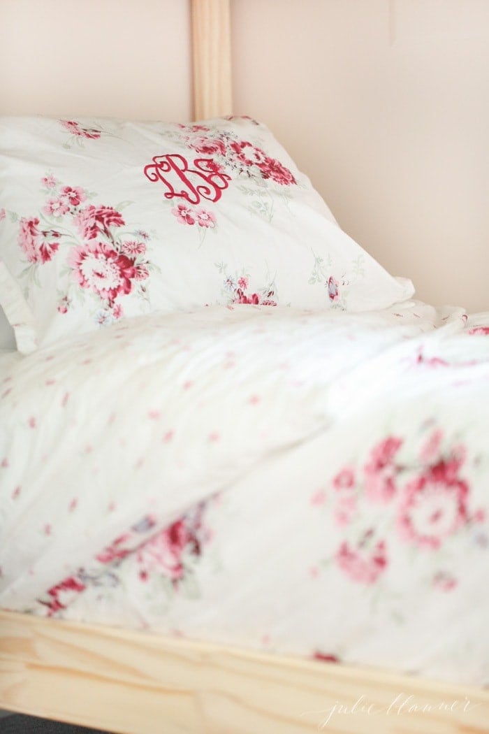 A close up of feminine pink bedding next to a solid wood bunk bed frame.