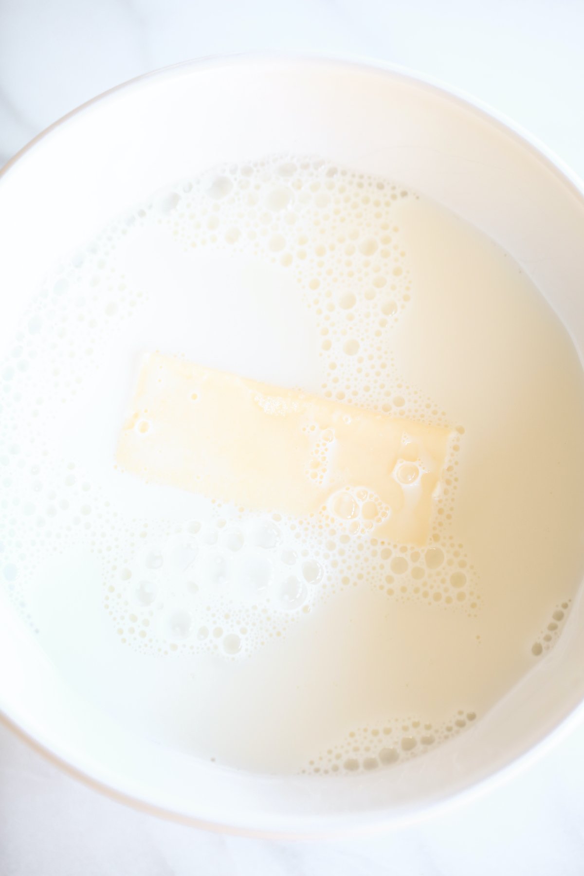 A stick of butter inside a bowl of milk.
