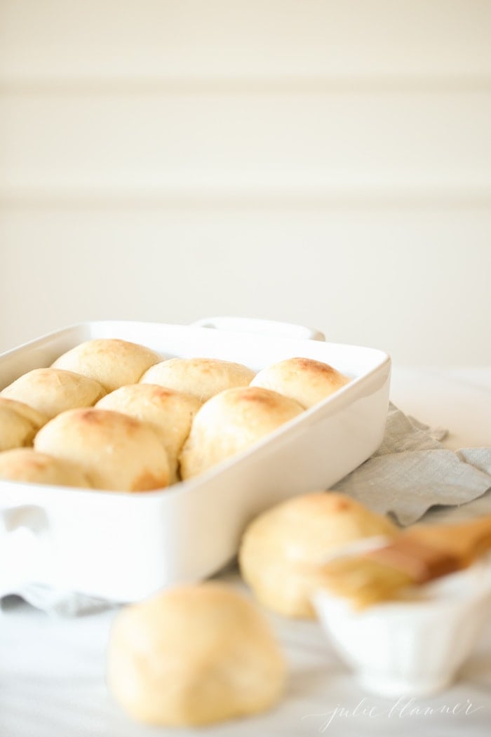 A white baking pan filled with homemade dinner rolls, two dinner rolls to the side. 