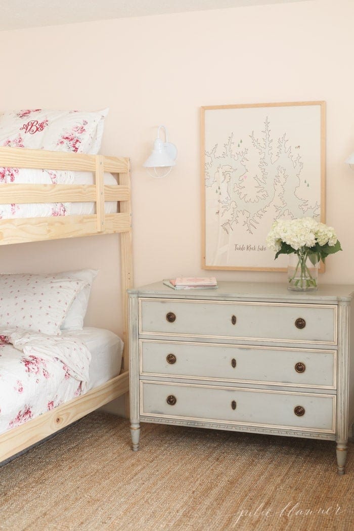 A soft pink bedroom with wooden bunk beds and feminine pink floral bedding.