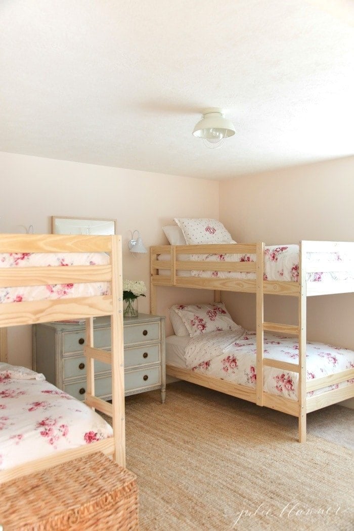 A soft pink bedroom with wooden bunk beds and feminine pink floral bedding.