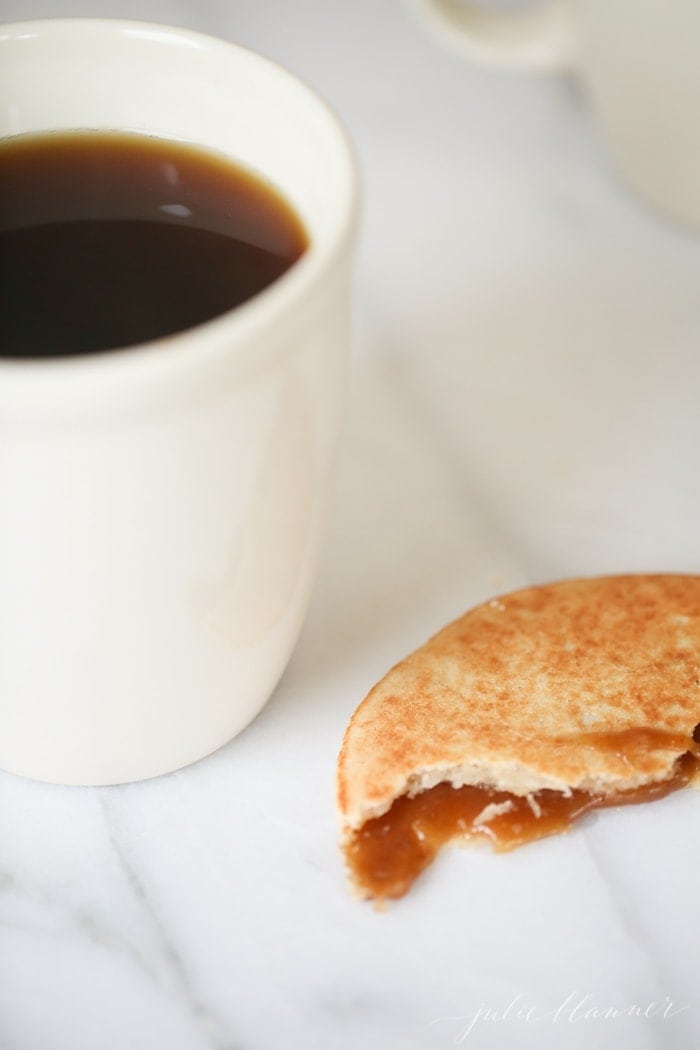 a stroopwafel with bites taken out, cup of coffee in the background
