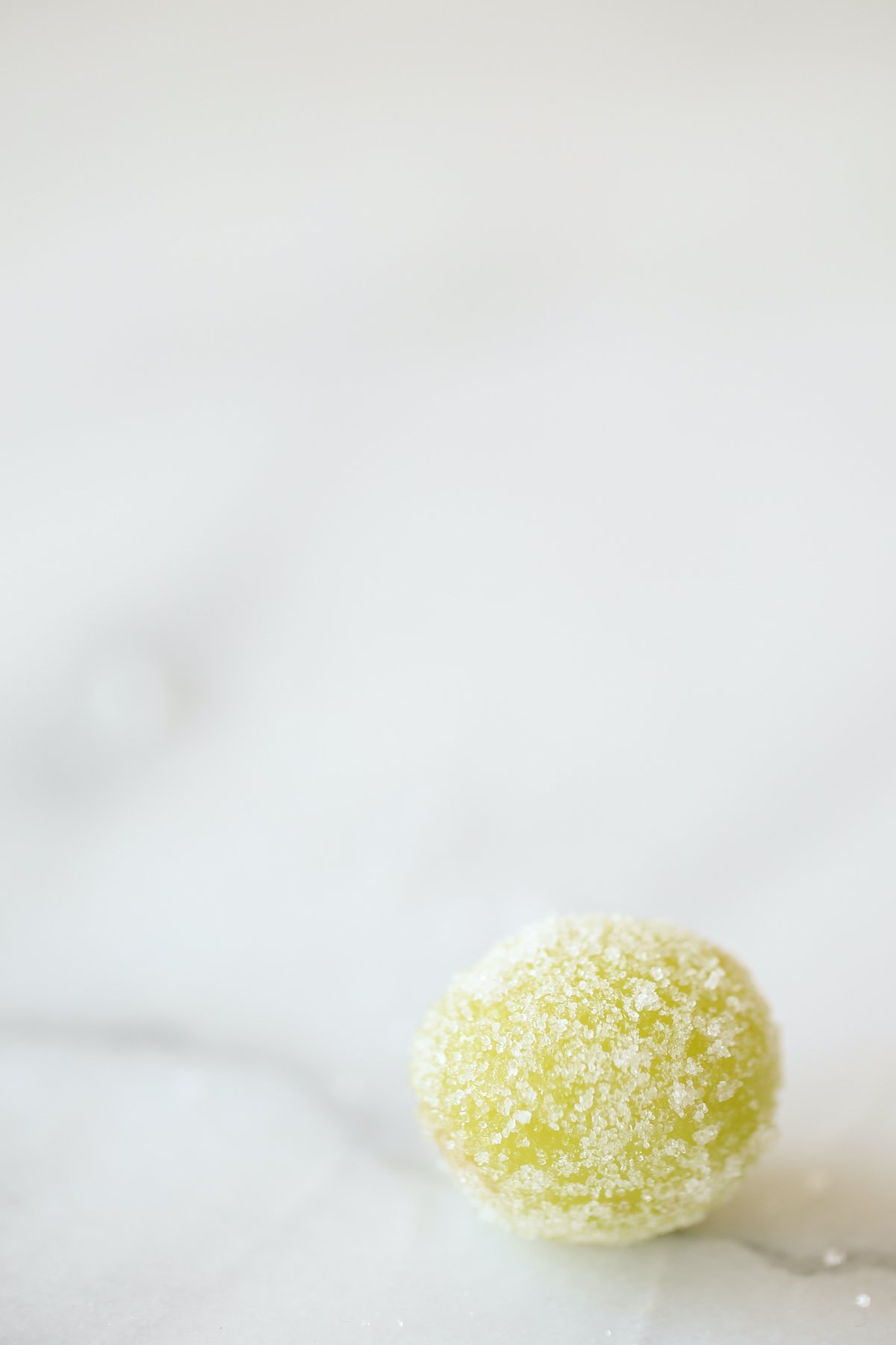 A single champagne grape, rolled in sugar on a marble countertop.