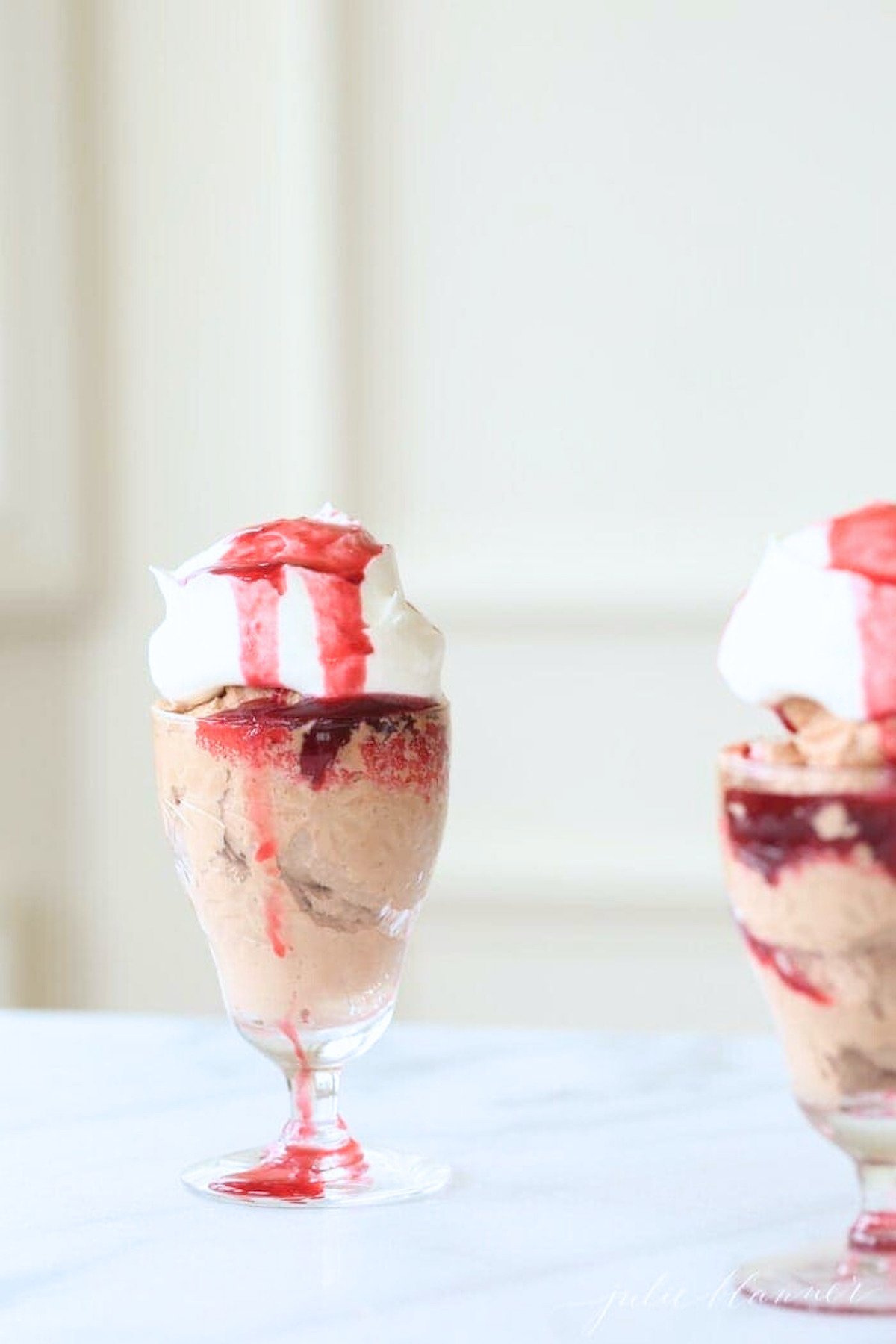 Two glasses with easy chocolate mousse topped with whipped cream and raspberry sauce.