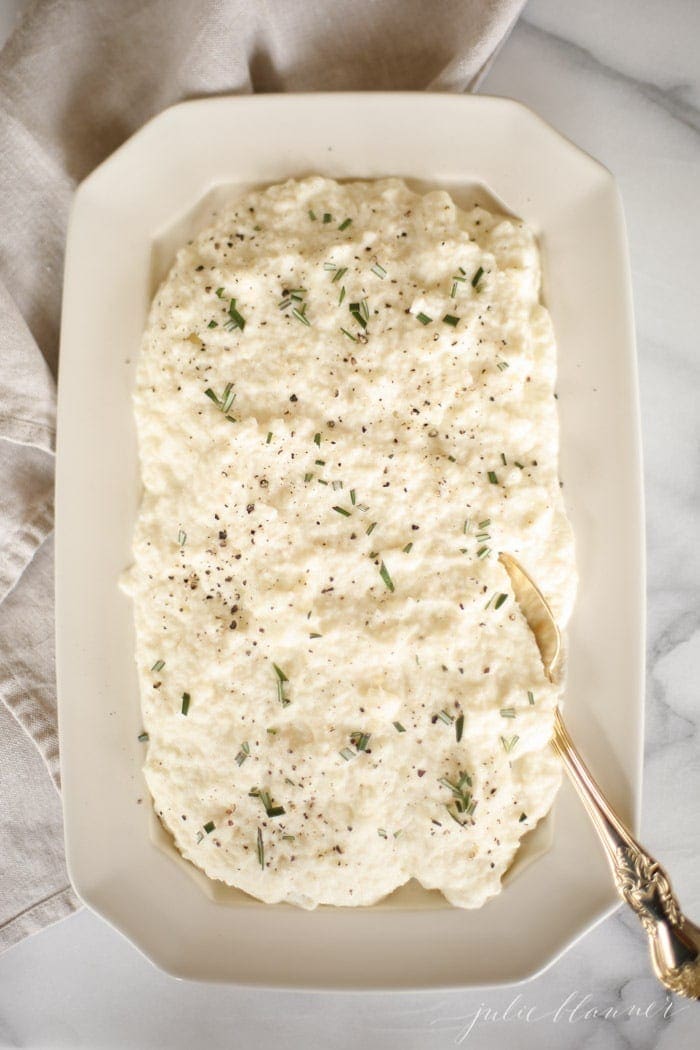 cauliflower mashed potatoes with rosemary in a white platter with gold spoon