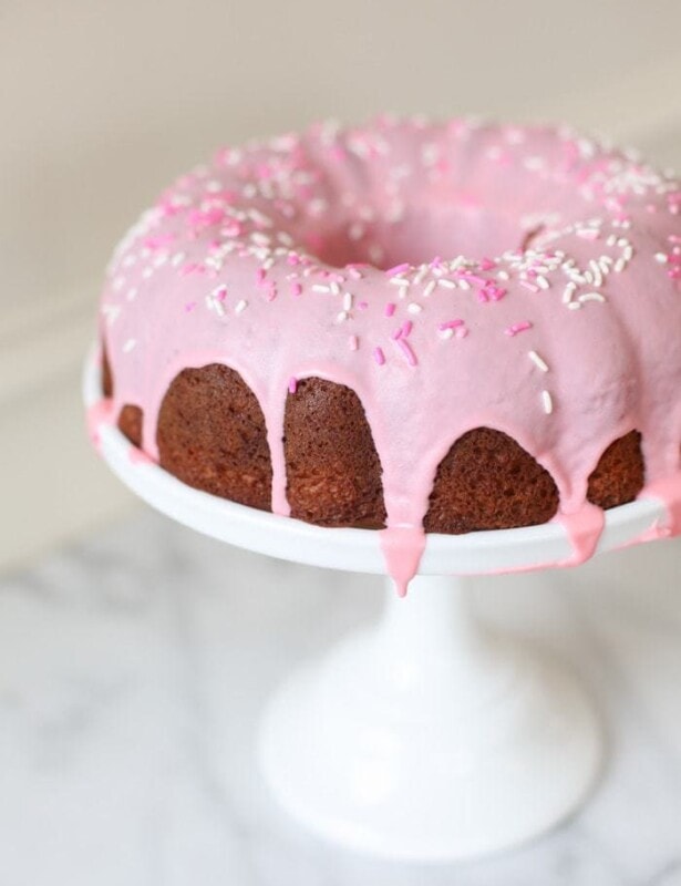 pink glazed donut cake with sprinkles on a white cake stand