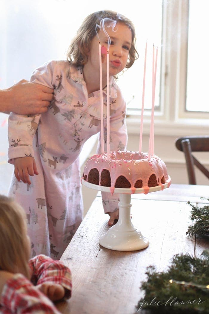 girl blowing candles on a glazed donut cake