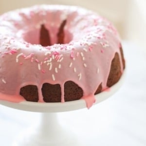 pink glazed donut cake with sprinkles on a white cake stand