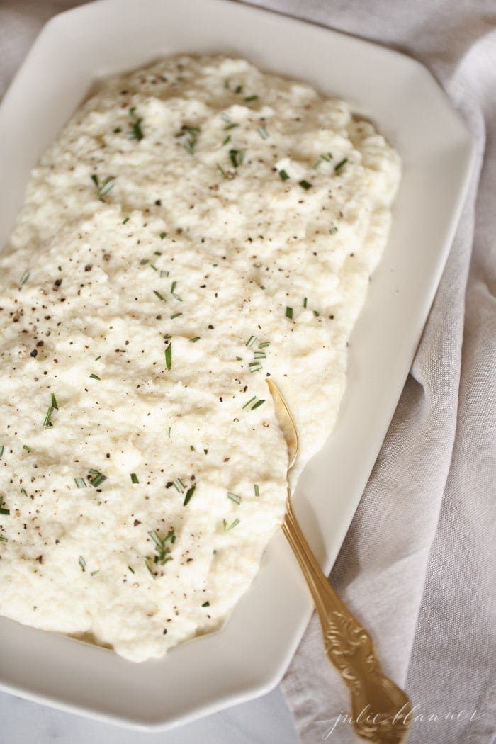 cauliflower mashed potatoes with rosemary in a white platter with gold spoon