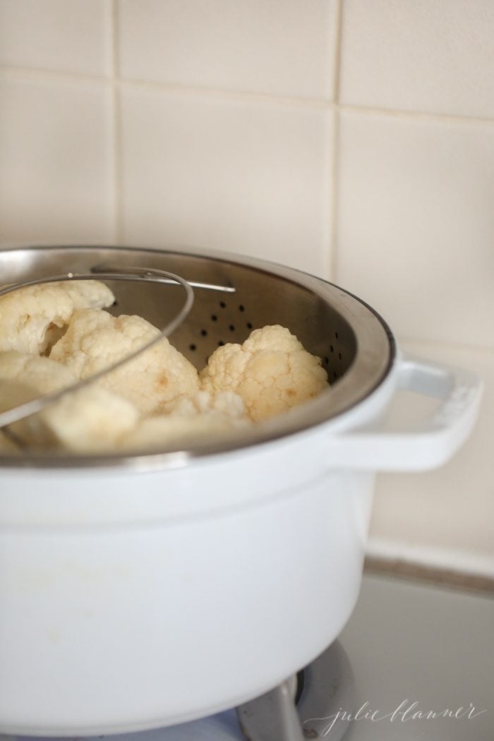 cauliflower in a steamer in a white ceramic dutch oven
