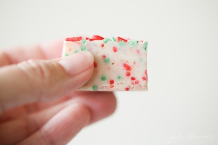 A hand holding a slice of white fudge with sprinkles