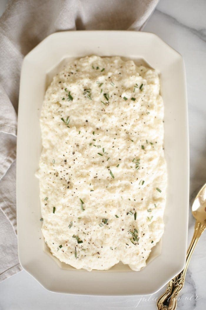cauliflower mashed potatoes with rosemary in a white platter with gold spoon