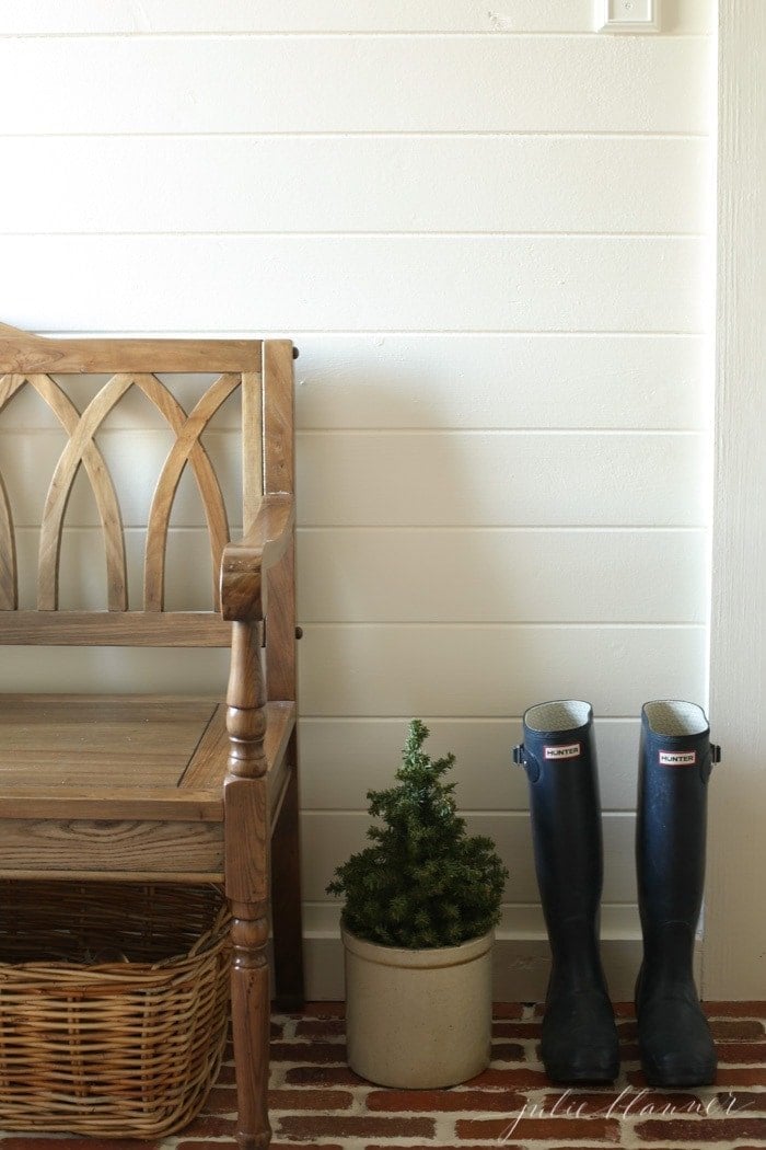 A mudroom with a wooden bench and Hunter boots, a small evergreen tree in a crock for winter decor.
