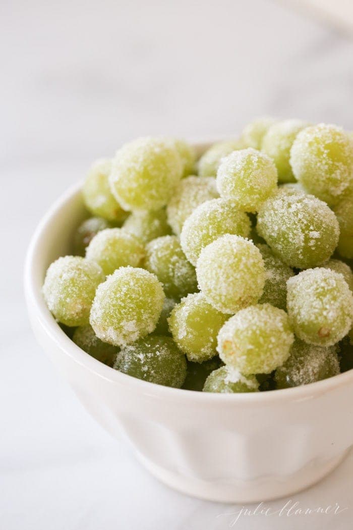 A white bowl of green grapes, soaked in champagne and rolled in sugar for New Year's Eve