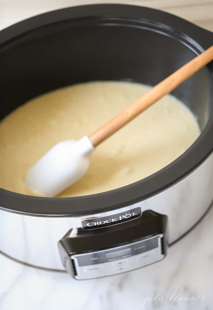 Crockpot fudge in the making, with melted white chocolate fudge inside, spatula stirring.