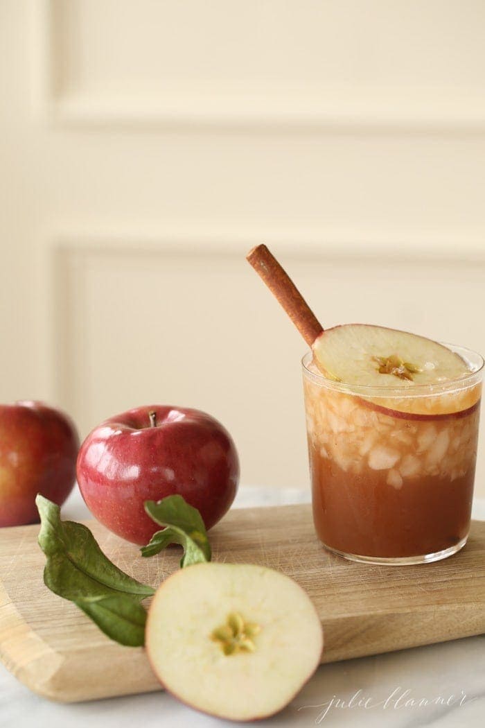 an apple cinnamon old fashioned made with apple butter in a clear glass, apples in the background.