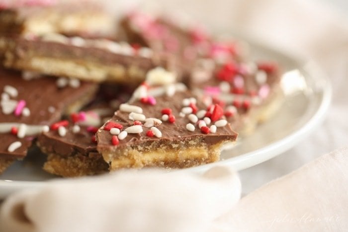 homemade toffee made from melted chocolate and saltines, sprinkled with Valentine's sprinkles on a white plate.