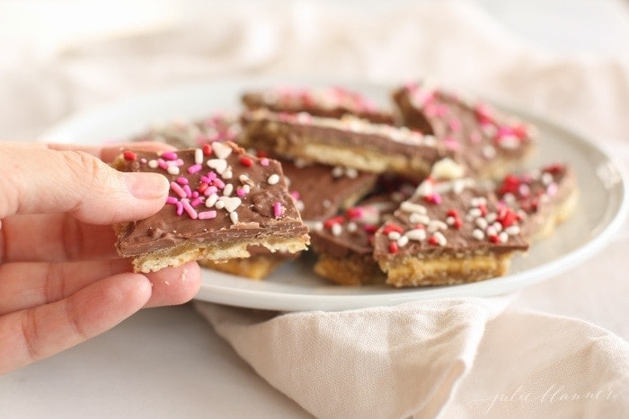 homemade toffee made from melted chocolate and saltines, sprinkled with Valentine's sprinkles on a white plate.