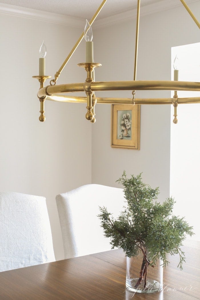 A brass chandelier over fresh greens for winter decor in a dining room.