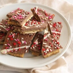 Easy toffee made with saltines, decorated with valentine's sprinkles on a white plate.