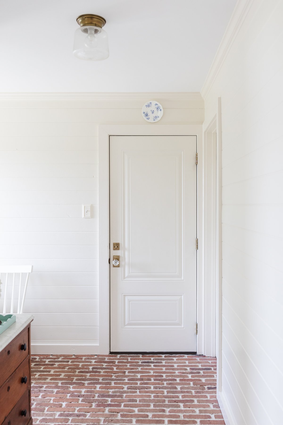 A mudroom with white wood paneled walls and brick flooring.
